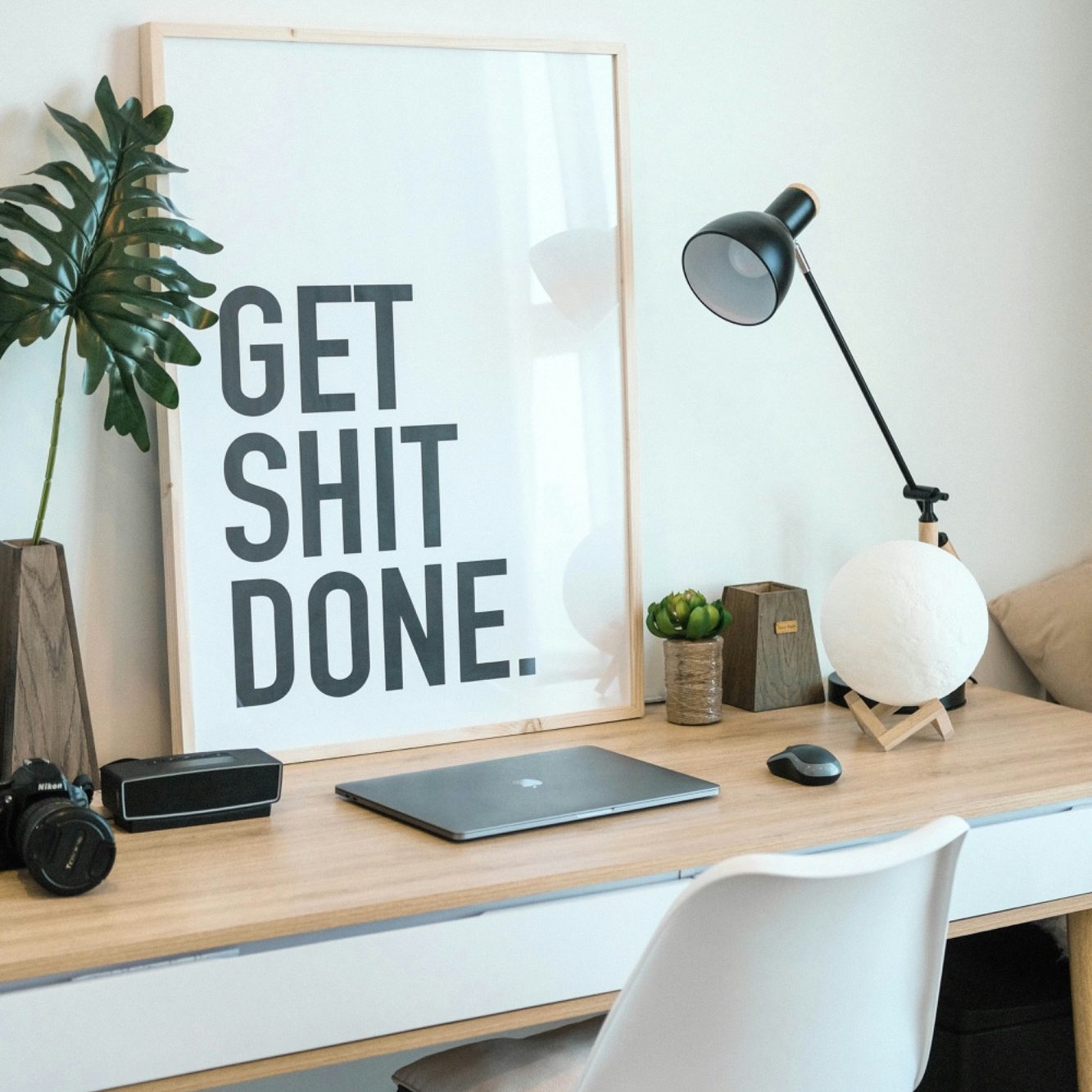 Schreibtisch mit Laptop, Lampe, Pflanze und Poster mit dem Spruch "GET SHIT DONE."