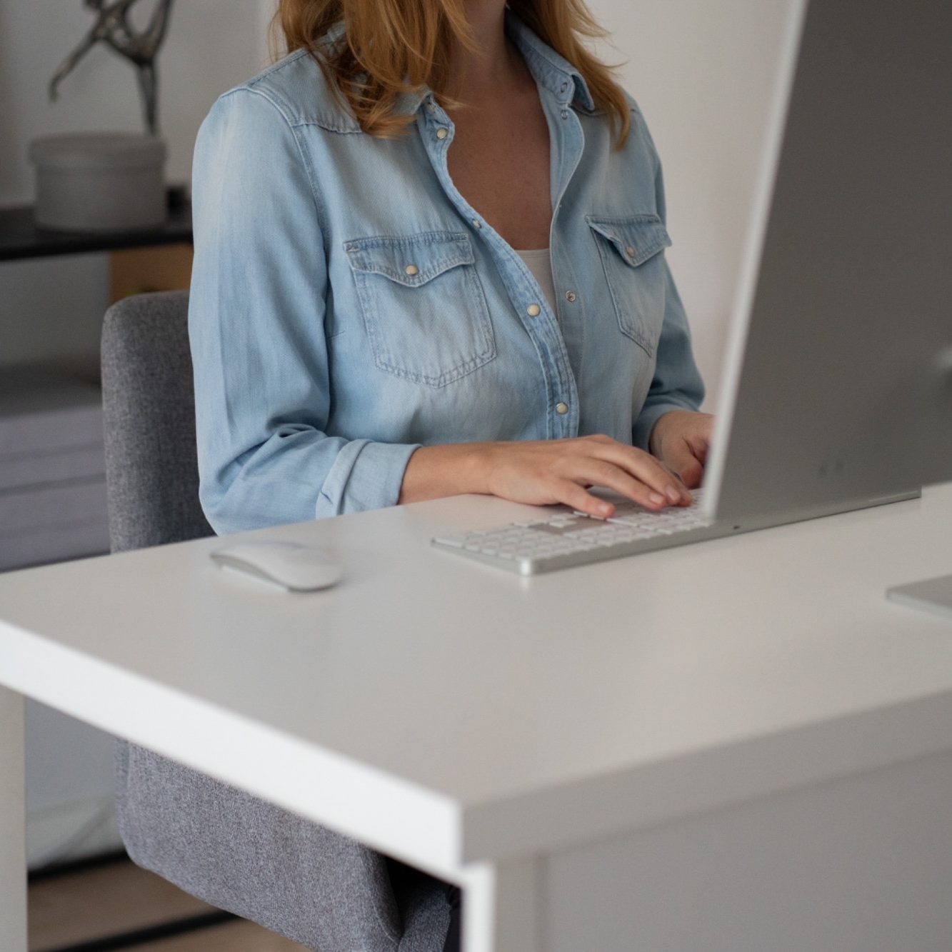 Frau in Bluse sitzt an einem Schreibtisch und arbeitet am Computer.
