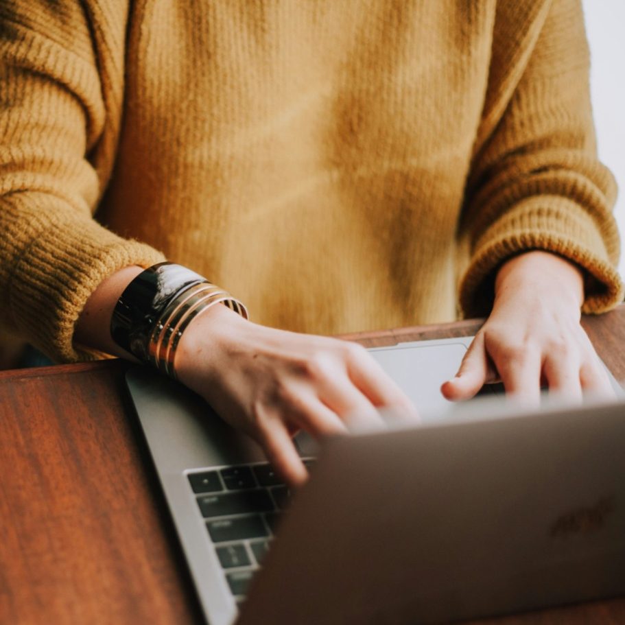 Eine Person in einem gelben Pullover tippt auf einem Laptop.